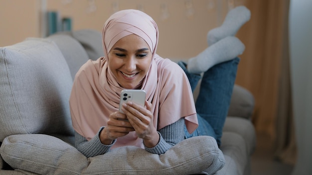 Giovane ragazza musulmana araba attraente donna islamica sdraiata sul divano di casa felice signora libanese indossa l'hijab