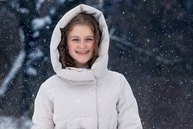 Giovane ragazza nella foresta invernale durante una nevicata. Ritratto di una giovane ragazza felice nella foresta invernale