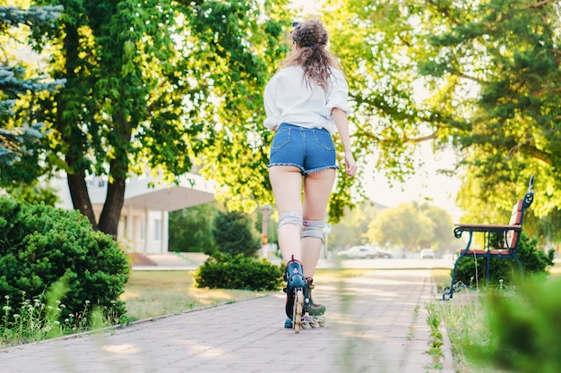 Giovane ragazza piacevole che pattina nel parco. avvicinamento. Concetto di riposo e divertimento