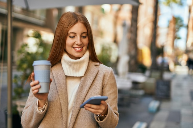 Giovane ragazza rossa che utilizza smartphone che beve caffè in città.