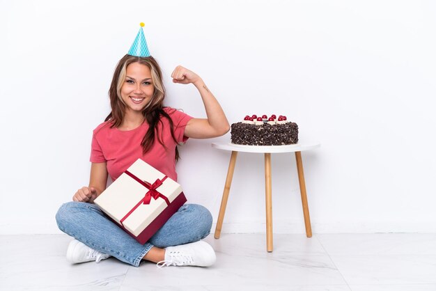 Giovane ragazza russa che festeggia un compleanno seduta sul pavimento isolato su sfondo bianco facendo un gesto forte