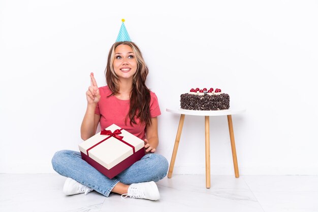 Giovane ragazza russa che festeggia un compleanno seduto sul pavimento isolato su sfondo bianco con le dita incrociate e augurando il meglio