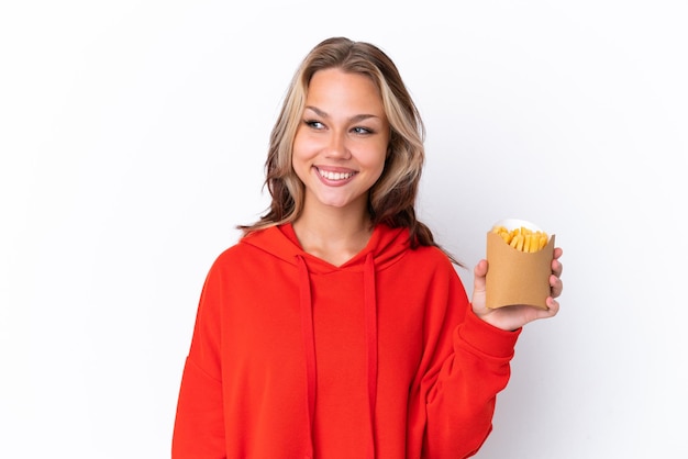 Giovane ragazza russa che tiene patatine fritte isolate su sfondo bianco guardando al lato e sorridente
