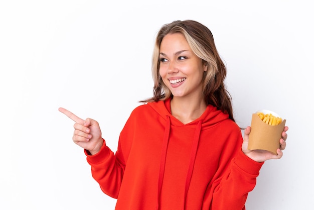 Giovane ragazza russa con patatine fritte isolate su sfondo bianco che punta il dito di lato e presenta un prodotto