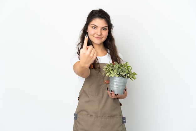 Giovane ragazza russa del giardiniere che tiene una pianta isolata facendo il gesto venente