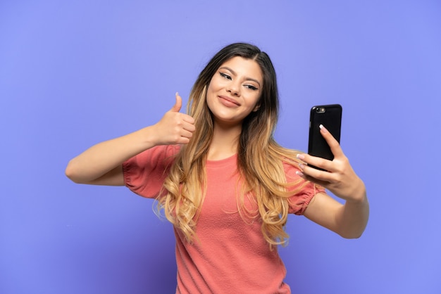 Giovane ragazza russa isolata su sfondo blu facendo un selfie con il cellulare