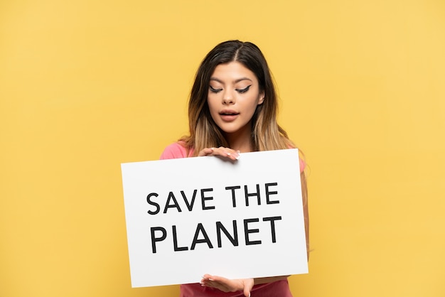 Giovane ragazza russa isolata su sfondo giallo in possesso di un cartello con testo Save the Planet