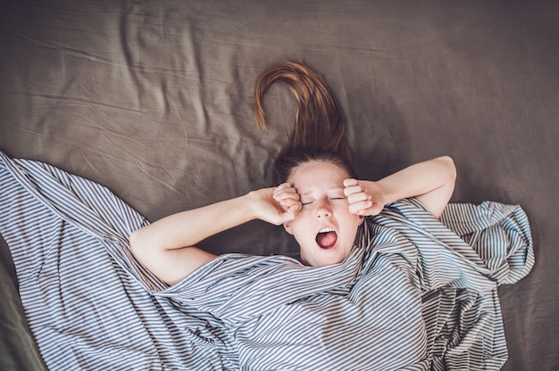 Giovane ragazza sdraiata a letto sotto una coperta