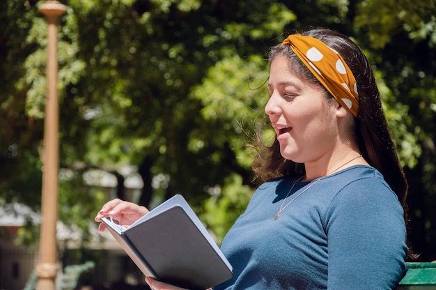 Giovane ragazza seduta nel parco a leggere e sorpresa