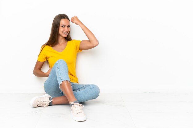 Giovane ragazza seduta sul pavimento facendo un gesto forte