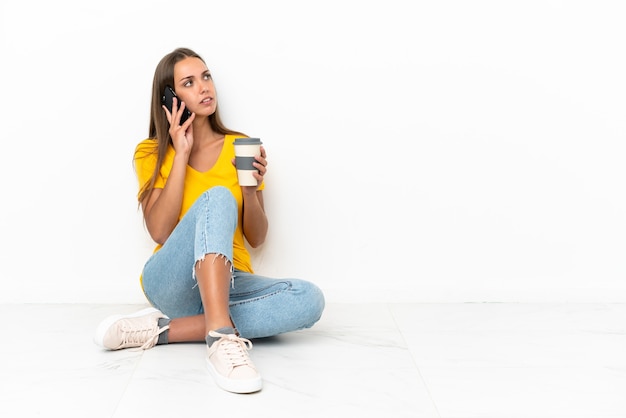 Giovane ragazza seduta sul pavimento tenendo il caffè da portare via e un cellulare