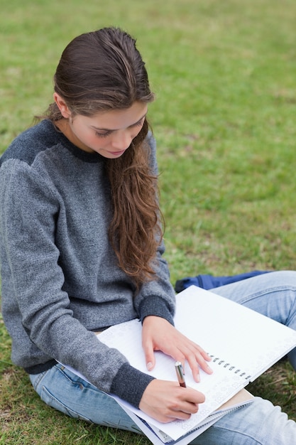 Giovane ragazza seria che fa i suoi compiti mentre sedendosi sull&#39;erba