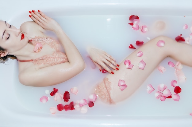 Giovane ragazza sexy che prende un bagno del latte con i petali di rosa