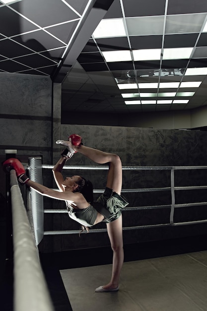 Giovane ragazza sexy in guantoni da boxe e abbigliamento sportivo facendo stretching sul ring