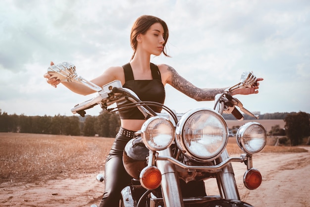 Giovane ragazza sexy in posa su una moto al tramonto. concetto di sport motoristico. Tecnica mista