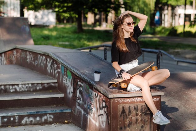 Giovane ragazza skater che riposa con uno skateboard nel parco dei pattinatori