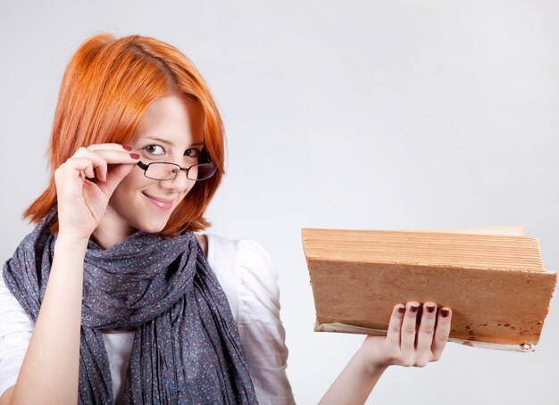 Giovane ragazza sorridente di moda in bicchieri con il libro di età.