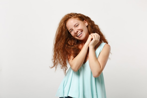 Giovane ragazza sorridente divertente rossa della donna in vestiti leggeri casuali che posano isolato sul ritratto bianco dello studio del fondo. Concetto di stile di vita di emozioni sincere della gente. Mock up copia spazio. Tenendo le mani giunte.