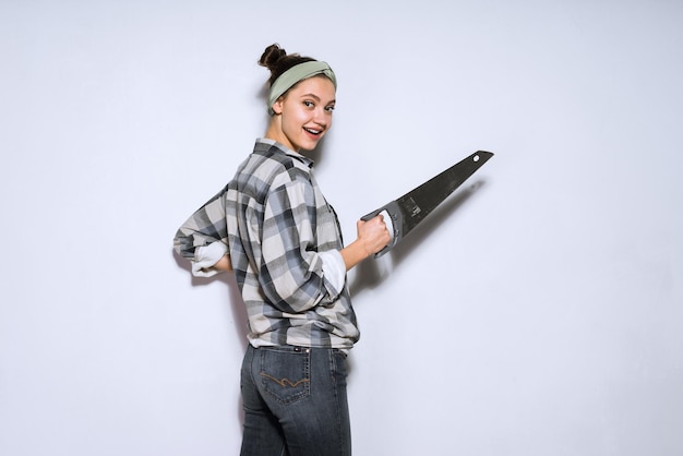 Giovane ragazza sorridente in camicia a quadri che tiene la sega metallica affilata nelle mani di riparazione in appartamento