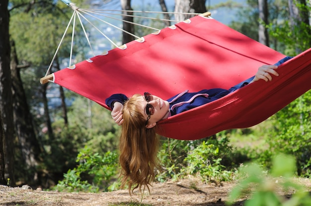 Giovane ragazza sorridente in un'amaca rossa nella foresta