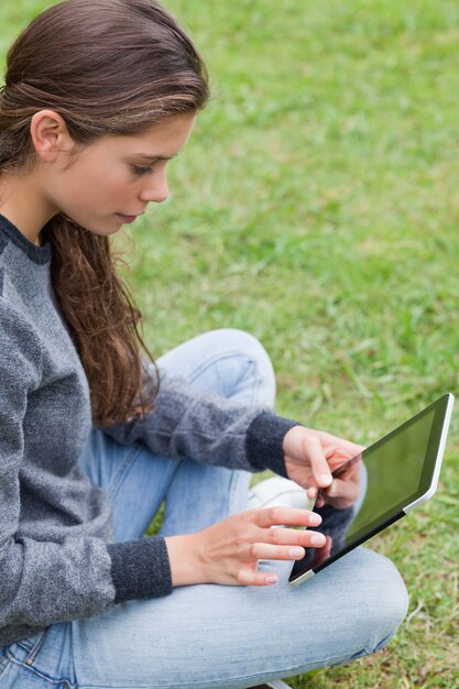 Giovane ragazza sorridente seduto a gambe accavallate mentre si tocca il suo tablet pc