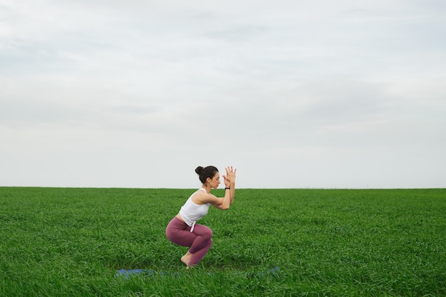 Giovane ragazza sottile che fa yoga all'aperto in un campo verde