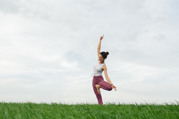 Giovane ragazza sottile che fa yoga all'aperto in un campo verde