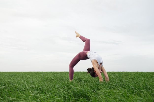 Giovane ragazza sottile che fa yoga all'aperto in un campo verde