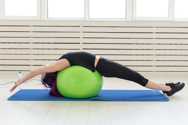 Giovane ragazza sottile fa esercizio e stretching per la schiena su un fitball verde nella luminosa palestra. Concetto di schiena e legamenti sani.