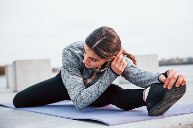Giovane ragazza sportiva che fa esercizi di yoga sul tappetino fitness all'aperto vicino al lago durante il giorno