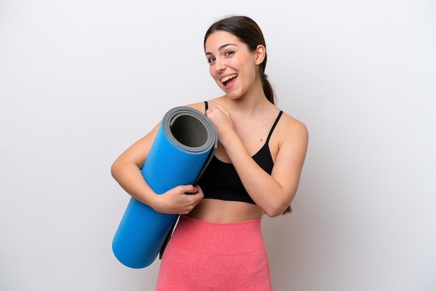 Giovane ragazza sportiva che va a lezioni di yoga tenendo un tappetino isolato su sfondo bianco che celebra una vittoria