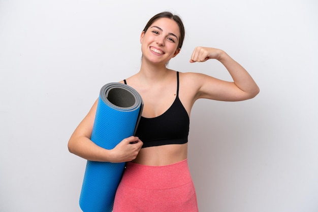 Giovane ragazza sportiva che va a lezioni di yoga tenendo un tappetino isolato su sfondo bianco facendo un forte gesto