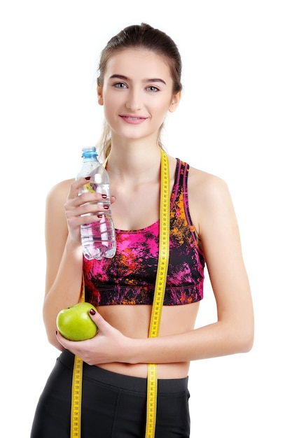 Giovane ragazza sportiva con acqua e mela di misurazione del nastro isolate