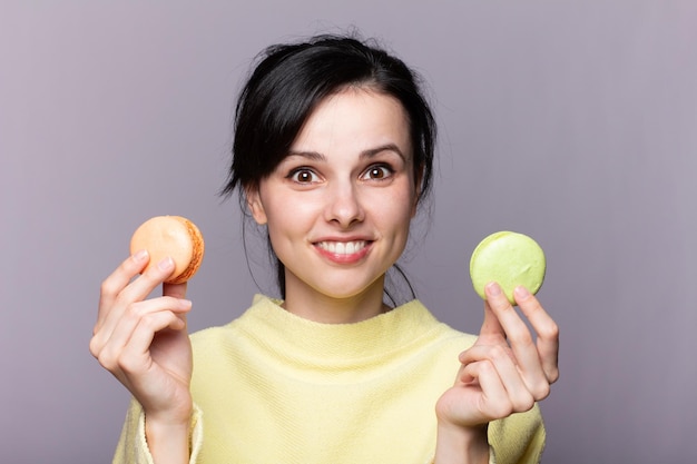 Giovane ragazza su sfondo grigio isolato che tiene colorati macarons francesi con espressione a sorpresa