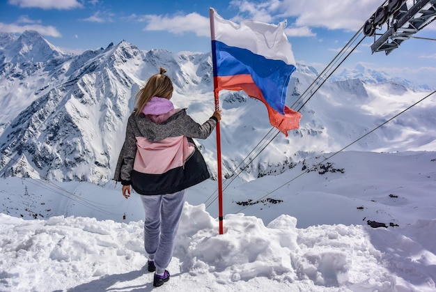 Giovane ragazza sullo sfondo delle montagne innevate e la bandiera della Russia Elbrus 25 aprile 2019