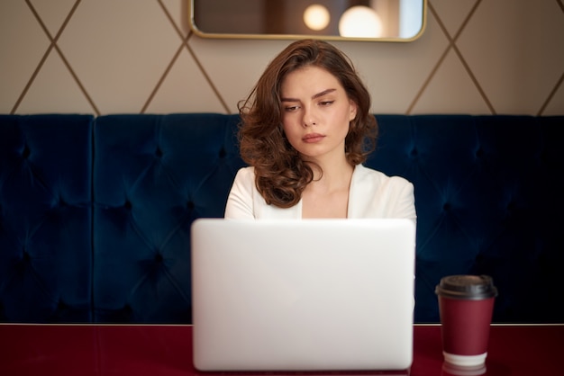 Giovane ragazza sveglia che lavora al computer portatile in caffè