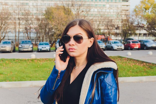 Giovane ragazza sveglia dello studente in vetri che parla sul telefono cellulare in parco.