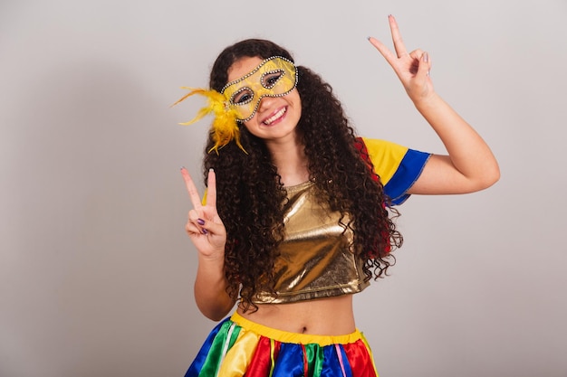 Giovane ragazza teenager brasiliana con vestiti frevo maschera di carnevale segno di pace e amore posa per foto primo piano foto