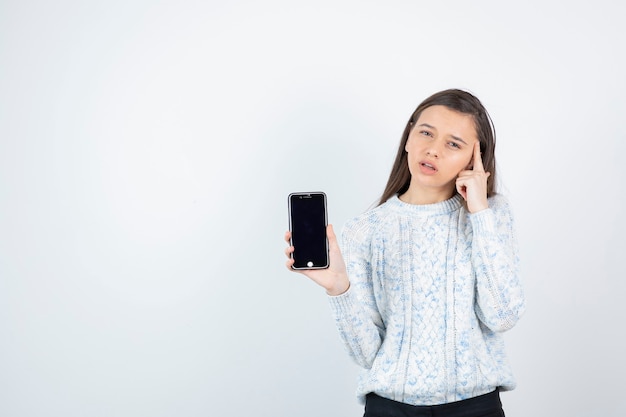 Giovane ragazza teenager che tiene smartphone su priorità bassa bianca.