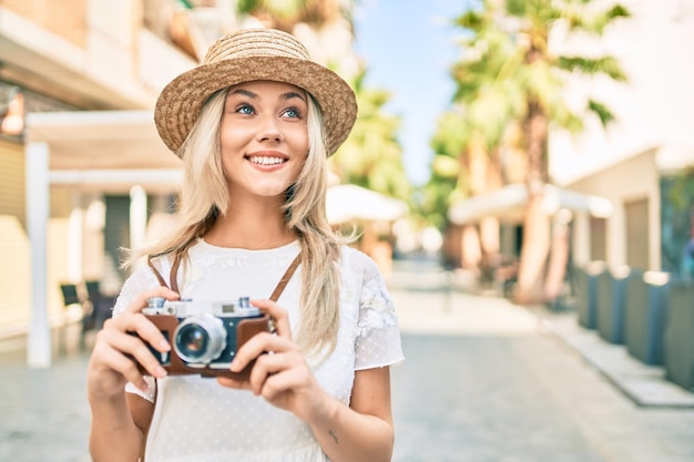 Giovane ragazza turistica caucasica che sorride felice usando la macchina fotografica d'epoca in strada della città.