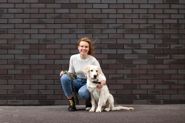Giovane ragazza urbana accarezza un cane per strada contro un muro