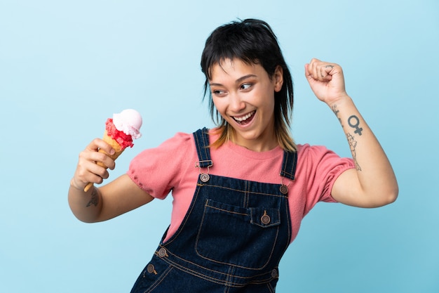 Giovane ragazza uruguaiana che tiene un gelato della cornetta sopra la parete blu che celebra una vittoria