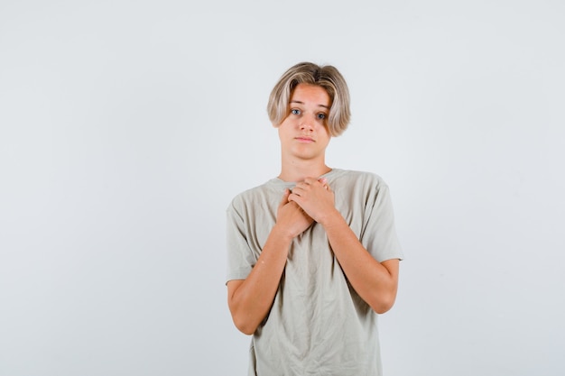 Giovane ragazzo adolescente che tiene le mani sul petto in maglietta e sembra deluso, vista frontale.