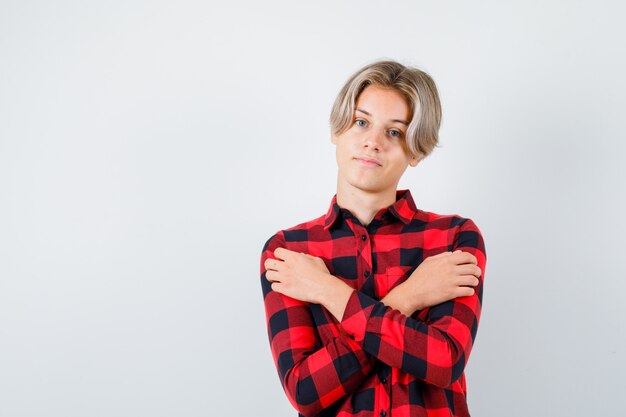 Giovane ragazzo adolescente in camicia a quadri che si abbraccia e sembra fiducioso, vista frontale.