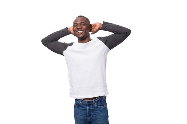 Giovane ragazzo africano gioioso vestito con una felpa bianca e nera e jeans su sfondo bianco