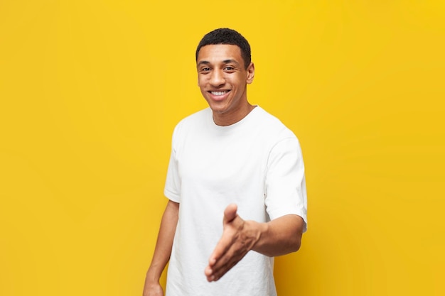 Giovane ragazzo afroamericano in maglietta bianca accoglie e invita su sfondo giallo isolato