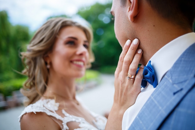 Giovane ragazzo alla moda nel costume dello sposo e della sposa bella ragazza in un vestito bianco con un treno a piedi nel parco il giorno delle nozze