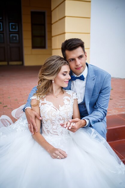 Giovane ragazzo alla moda nel costume dello sposo e della sposa bella ragazza in un vestito bianco con un treno a piedi nel parco il giorno delle nozze