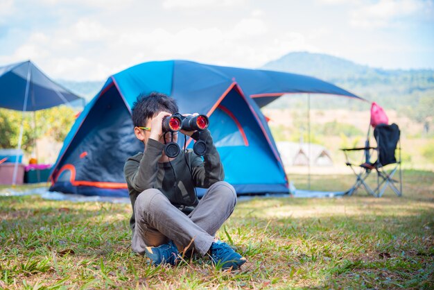 Giovane ragazzo asiatico che osserva con il binocolo nel campeggio