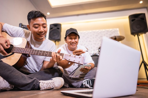 Giovane ragazzo asiatico che suona la chitarra e il suo amico che guarda un video musicale